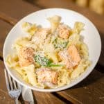 creamy salmon pasta in a white bowl on a wooden table and a silver knife and fork on the side