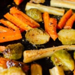 roasted carrots,parsnips and brussel sprouts with maple and rosemary glaze on a black baking tray