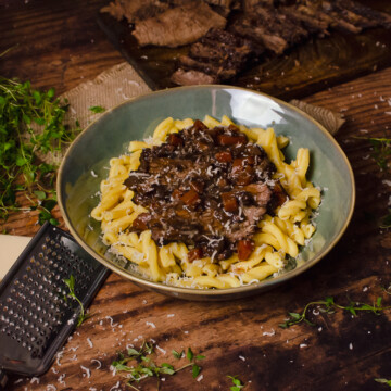 Italian Pot Roast with Pasta served in a green bowl with chopped beef,fresh thyme and a cheese grater in the background