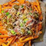 Loaded Vegan Sweet Potato Fries on a dark wooden board with grated Parmesan cheese on top