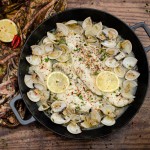 Haddock and Clams in Garlic and Wine Sauce in a cast iron pan on a wooden table with lemon and red chillies on a brown and pink towel