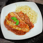 Chicken parmesan served with tomato passata sauce and spaghetti on a white plate