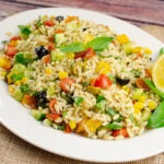 Fresh Orzo Pasta Salad served on a large white plate with fresh basil leaves and a lemon slice on the side