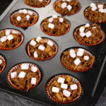 chocolate cornflake cake in orange cupcake cases in a metal cupcake tin with pink and white marshmallows sprinkled over the top