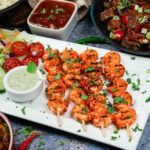 Tandoori King Prawn Skewers on a white plate with chopped fresh coriander sprinkled over the top with side salad on the side with mint raita
