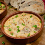 Cheesy Mushrooms in a Creamy Garlic Sauce in a tapas dish with crusty bread on the side