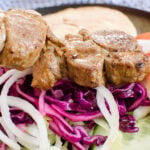 Lamb shish kebab being placed onto red cabbage salad