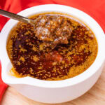 Chopped onion and garlic on a spoon whilst stirring the seafood boil sauce in a white dipping bowl