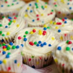 Vanillia cupcakes with buttercream frosting decorated with red green yellow and blue balls. In spotted cupcake cases.