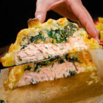 Salmon en croute cut in half with a slice showing the perfectly cooked salmon and filling.