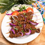 Suya Beef Kebabs served on a white platter plate with red onion,tomato,cucumber,white cabbage and chopped parsley sprinkled on top