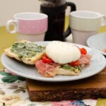 Italian styled eggs benedict served on pancetta bread with pesto cherry tomatoes and prosciutto and fresh coffee in the background