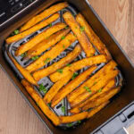 Cooked Air Fryer Sweet Potato Fries in an air fryer basket with chopped parsley sprinkled over the top