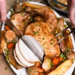 slicing slow cooker chicken which is served on a platter plate with peas, parsnips, carrots, onion and stuffing balls