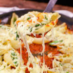 Picking up our Spinach and Ricotta Stuffed Shells with a black plastic spoon with melted cheese dripping down