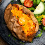 Jacket Sweet Potato in the air fryer cut open with chopped chives on top and a salad on the side