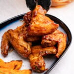 Air Fryer Chicken Wings in BBQ Sauce being placed onto a plate with sweet potato wedges
