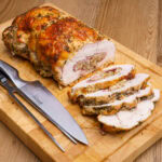 Rolled Turkey Breast Joint with Stuffing sliced on a wooden chopping board with a knife and carving fork on the side
