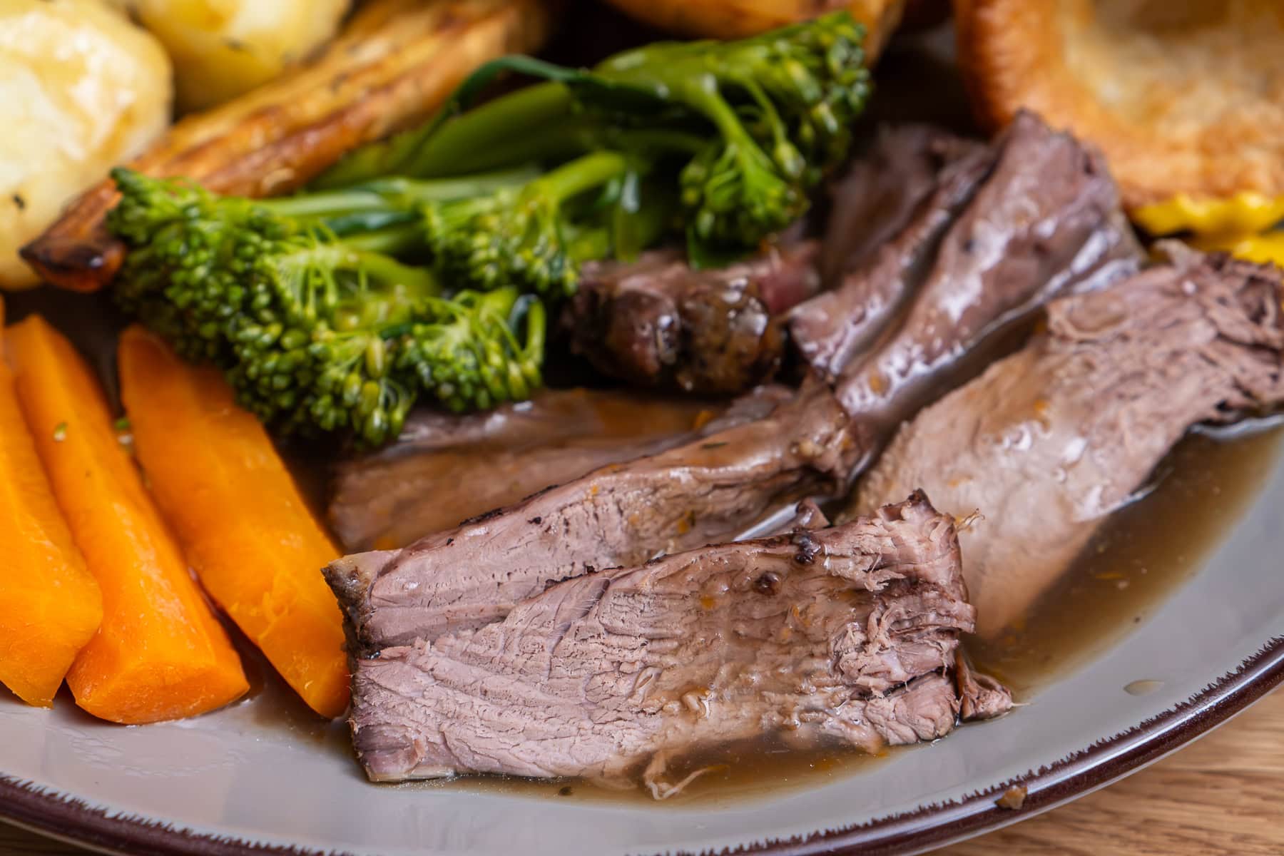 Slices of beef shin on a plate of roast dinner smothered in beef gravy