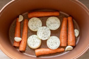 Sliced carrots, onions ,garlic cloves and thyme in a slow cooker pot