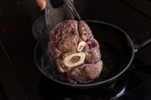 Searing the the beef shank in a frying pan holding the beef shin with tongs
