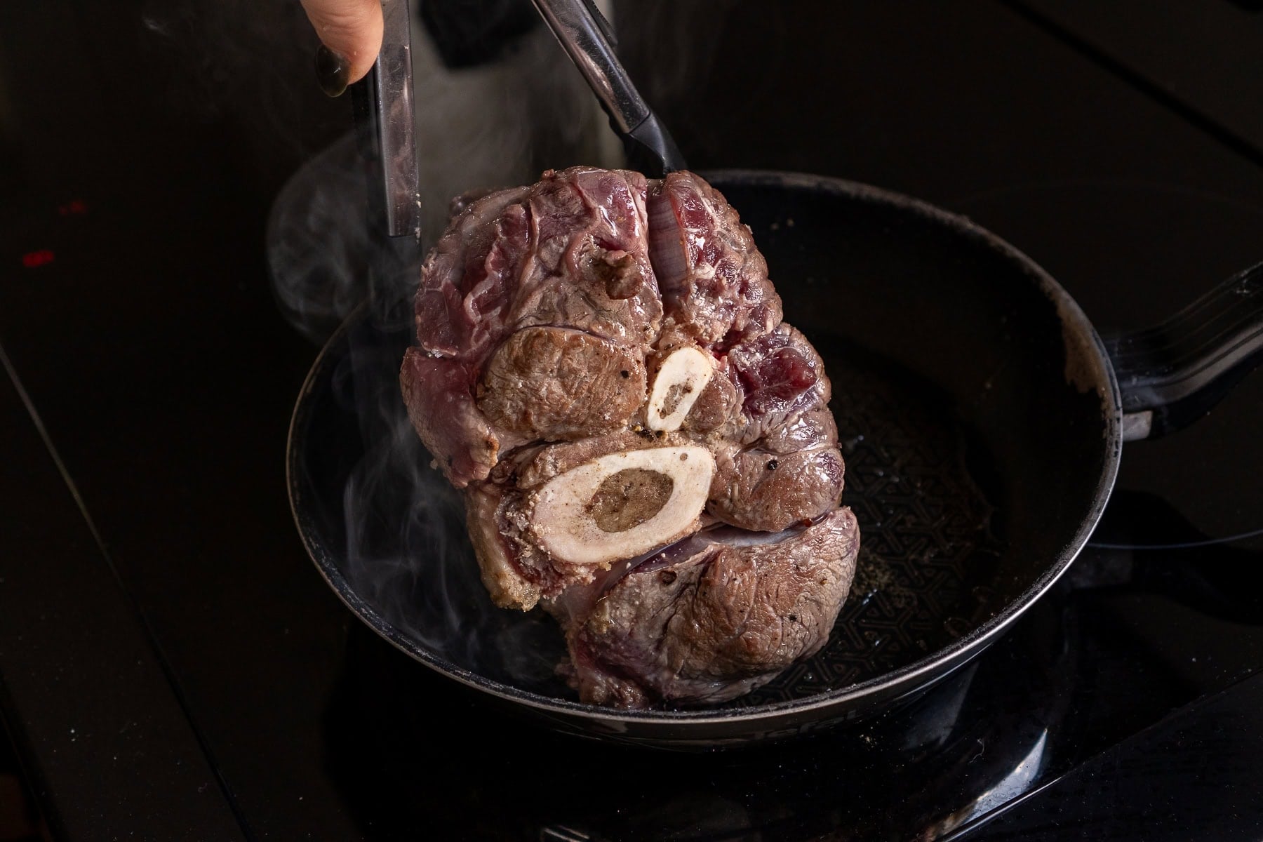 Searing the the beef shank in a frying pan holding the beef shin with tongs