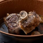 A cooked beef shin in a slow cooker on a vegetable trivet and gravy