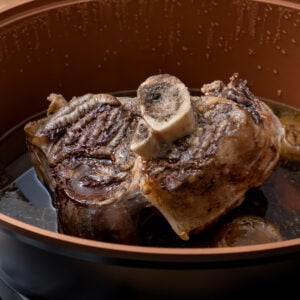 A cooked beef shin in a slow cooker on a vegetable trivet and gravy