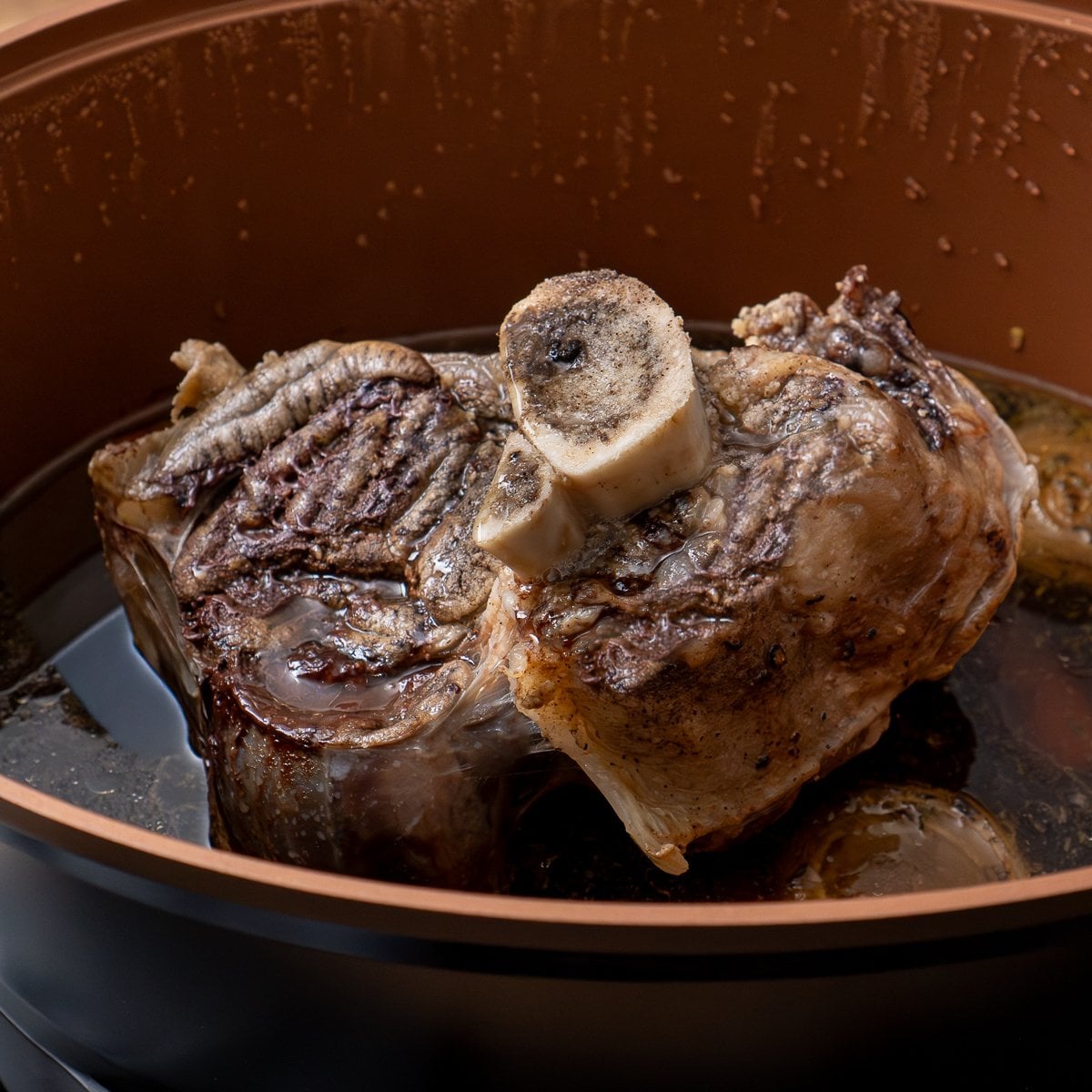 A cooked beef shin in a slow cooker on a vegetable trivet and gravy