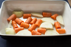 A vegetable trivet of chopped onion and carrot in a oven proof dish