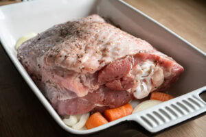 A turkey thigh coated in salt and pepper on a vegetable trivet in a oven proof dish
