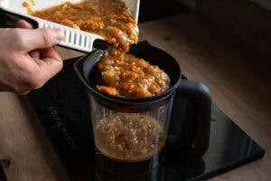 Pouring stock, crushed onions and carrots into a sieved jug