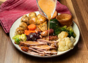 Pouring gravy over a turkey roast dinner which consists of turkey thigh, cauliflower, broccoli, Brussels stuffing balls, Yorkshire puddings and roast potatoes
