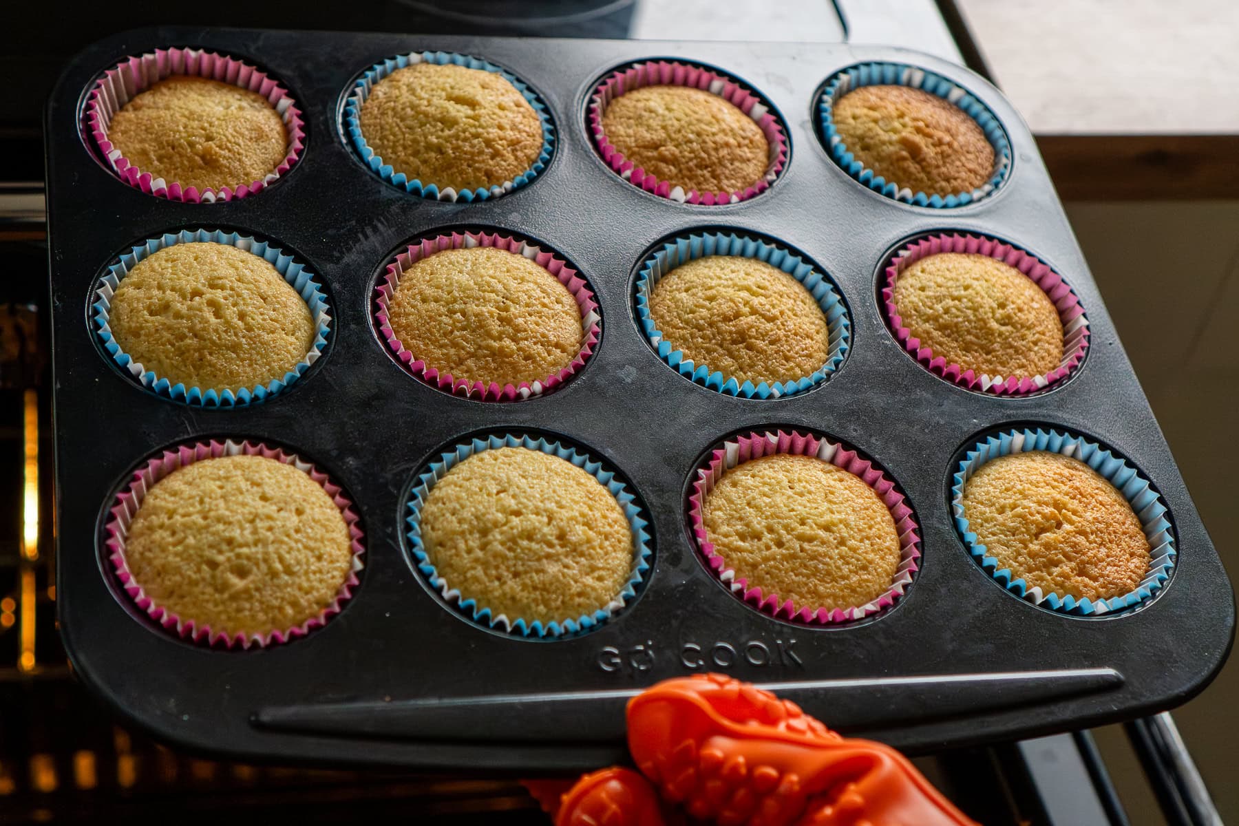 Twelve fairy cakes cooked in a tray coming out the oven