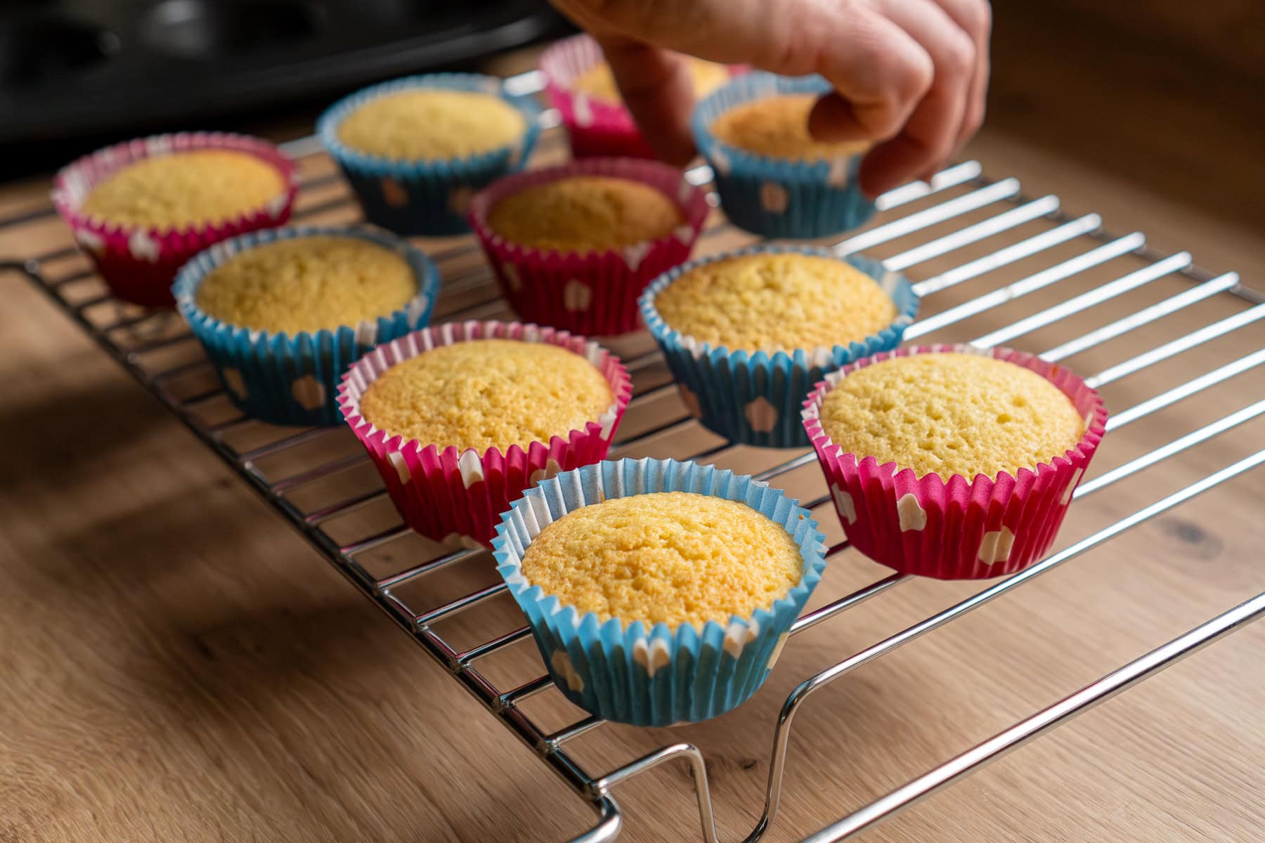 Placing cooked fairy cakes onto a wire rack to cool