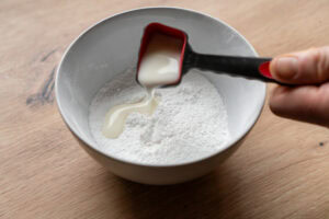Pouring a tablespoon of milk into a bowl of icing sugar