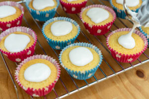 Fairy cakes on a wire rack with icing being put on top of each cake