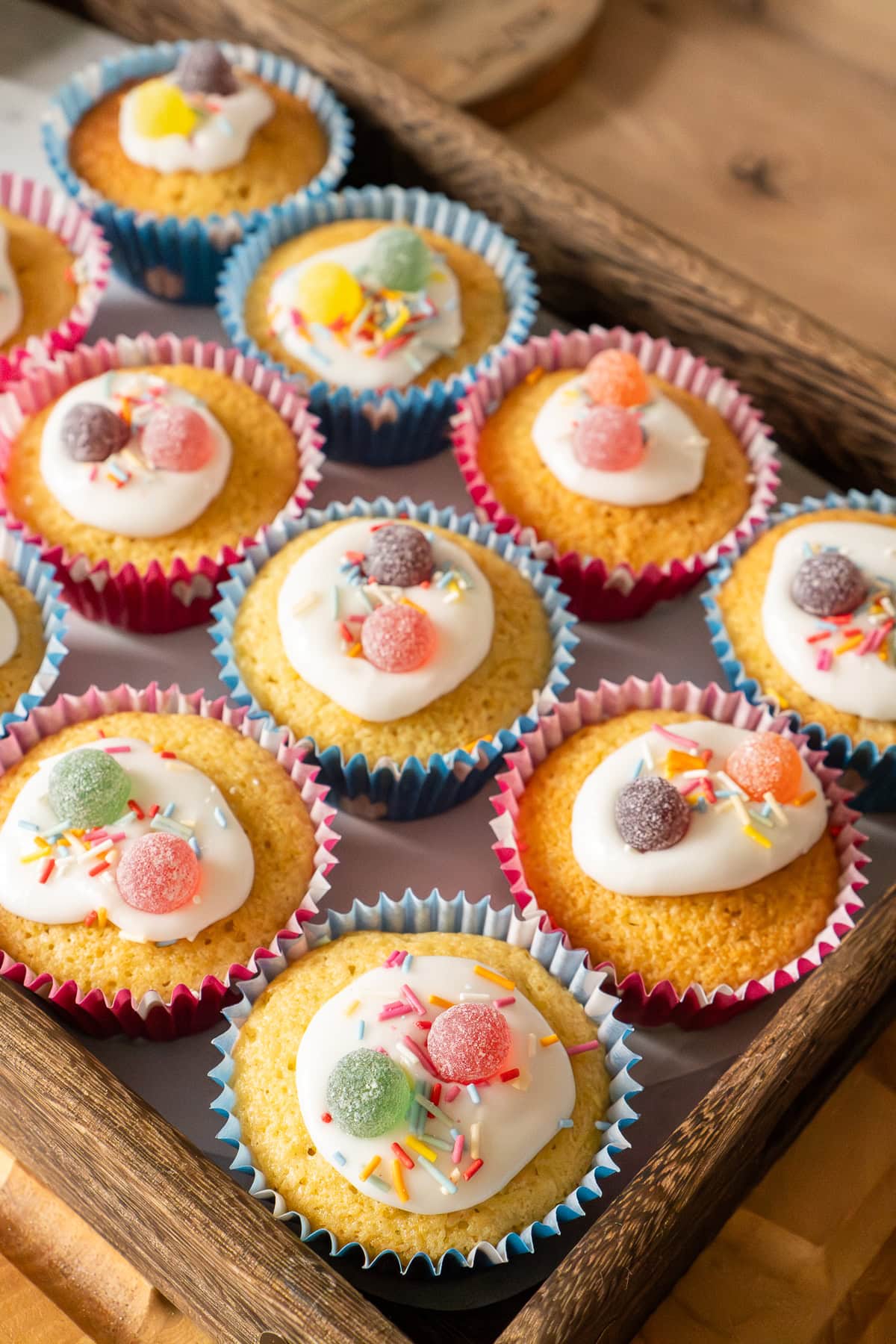 A tray of fairy cakes decorated in icing, sprinkles and sweets