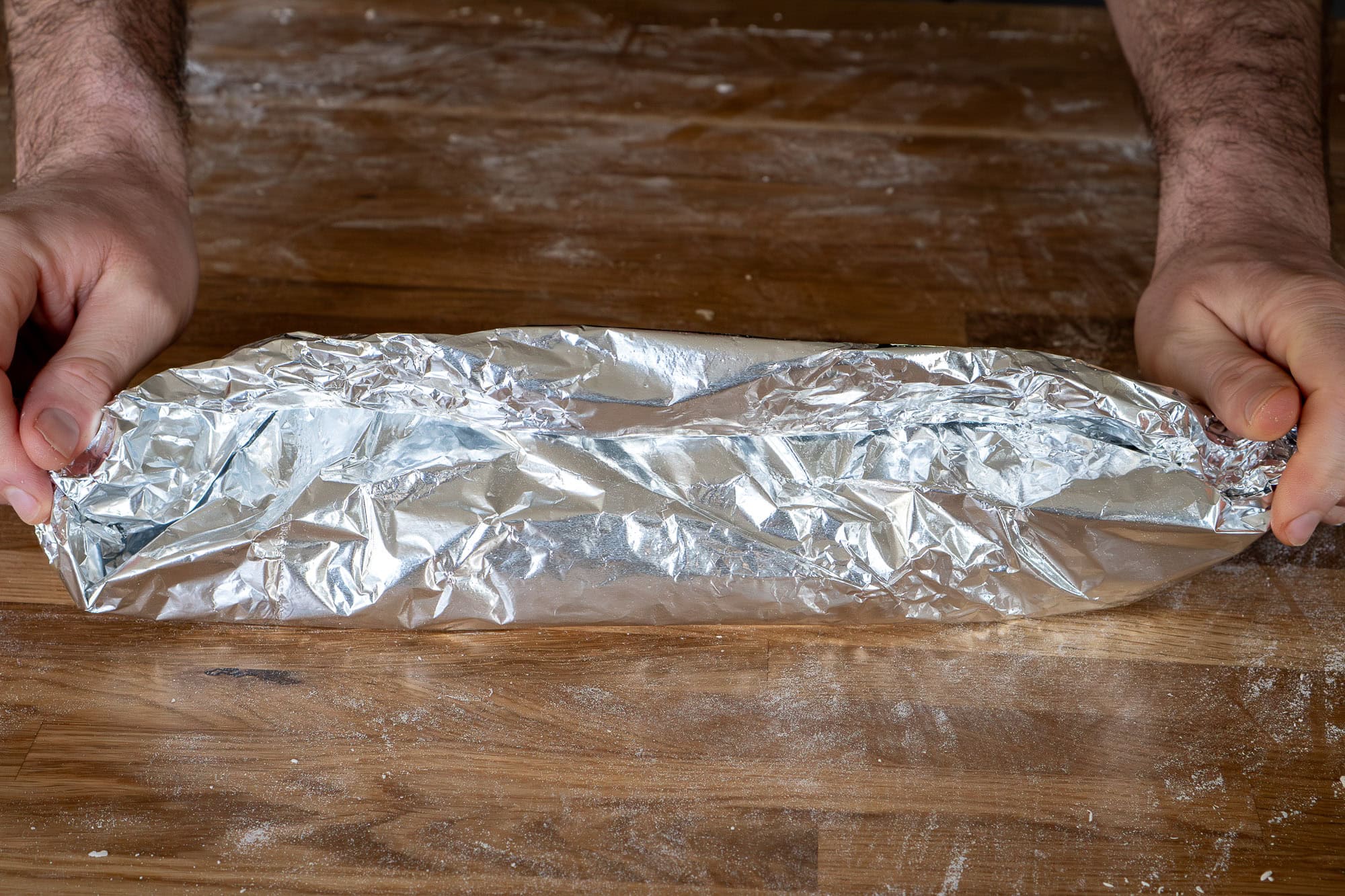 Wrapping the parchment paper round the roly poly forming a parcel closing the ends