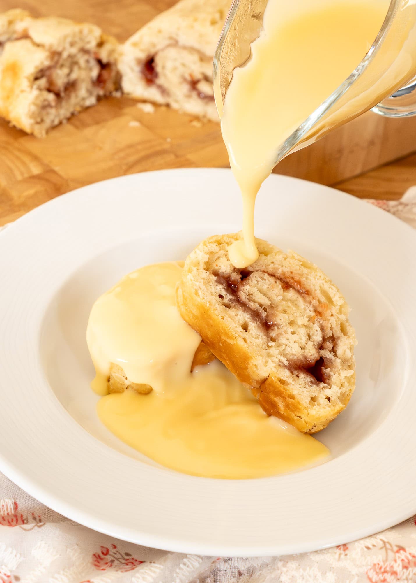 Pouring hot custard over jam roly poly in a bowl