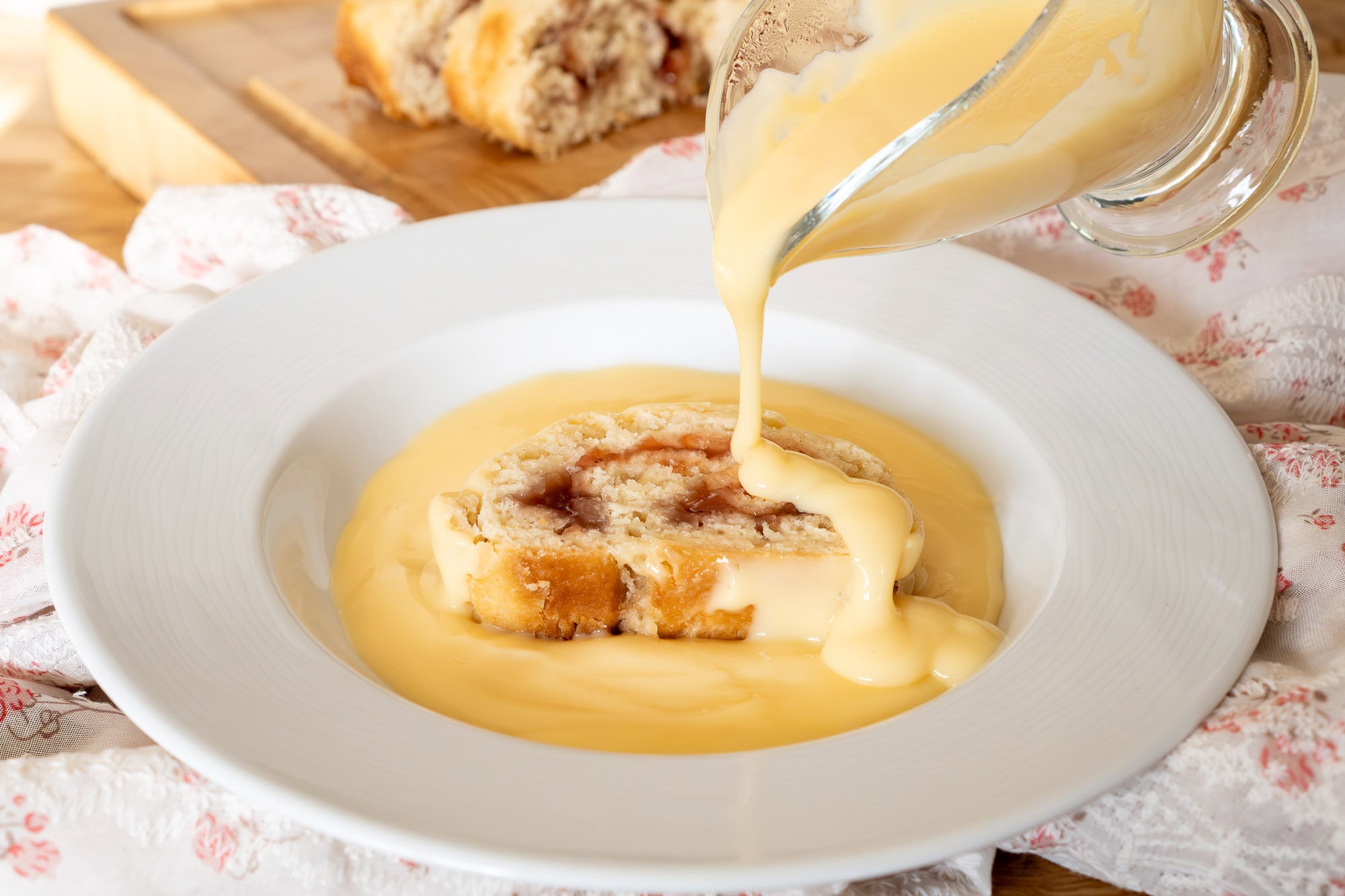 Pouring hot custard over jam roly poly in a bowl