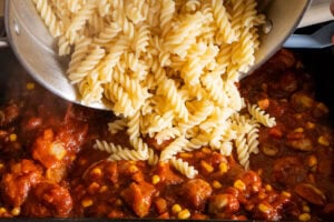 Pouring cooked pasta into sausage pasta bake tomato sauce