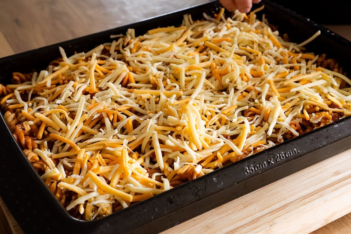 Putting grated cheese on top of the sausage pasta bake