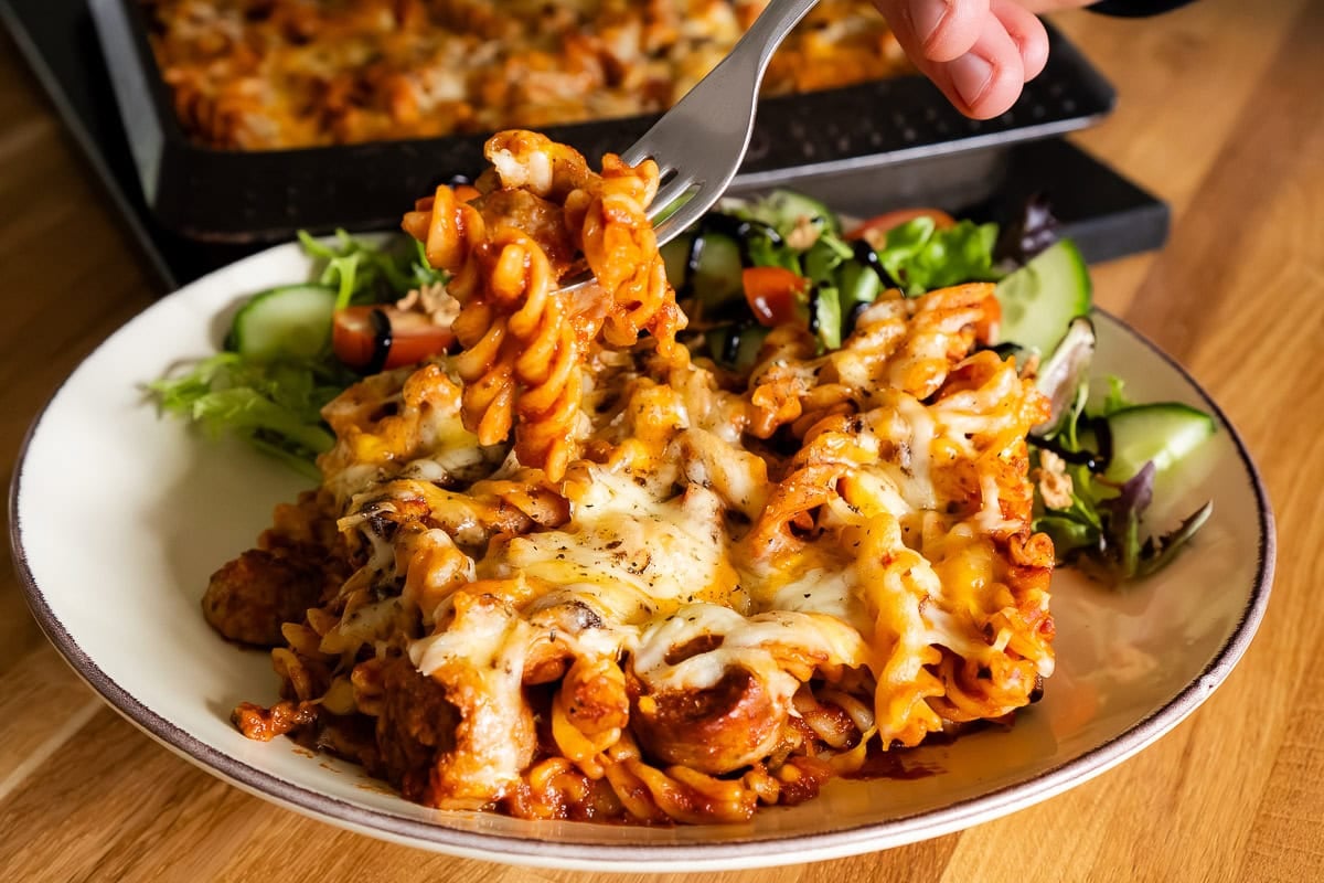 Sausage Pasta Bake on a plate with salad and being picked up with a fork