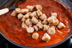 Adding chopped sausages to the tomato sauce