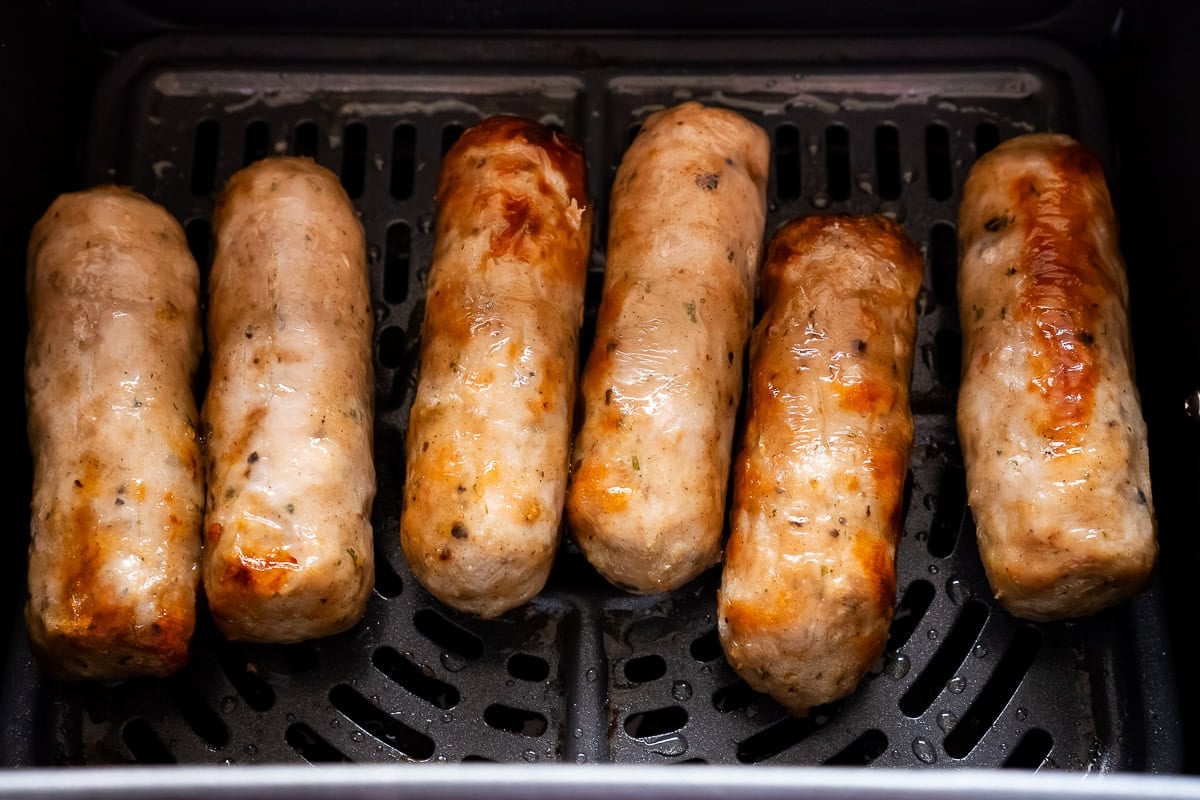 Six cooked sausages in an air fryer tray