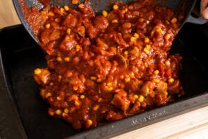 Pouring Sausage and Tomato Pasta sauce into a oven baking tray
