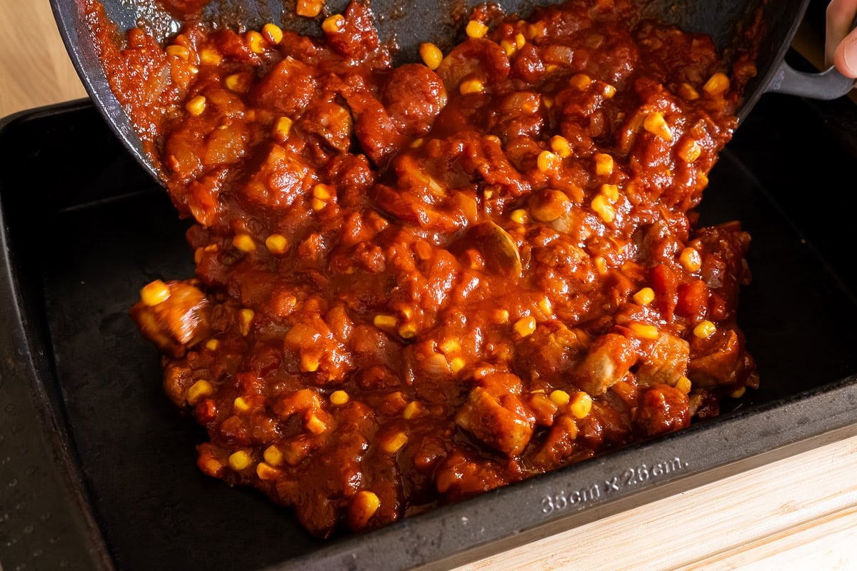 Pouring Sausage and Tomato Pasta sauce into a oven baking tray