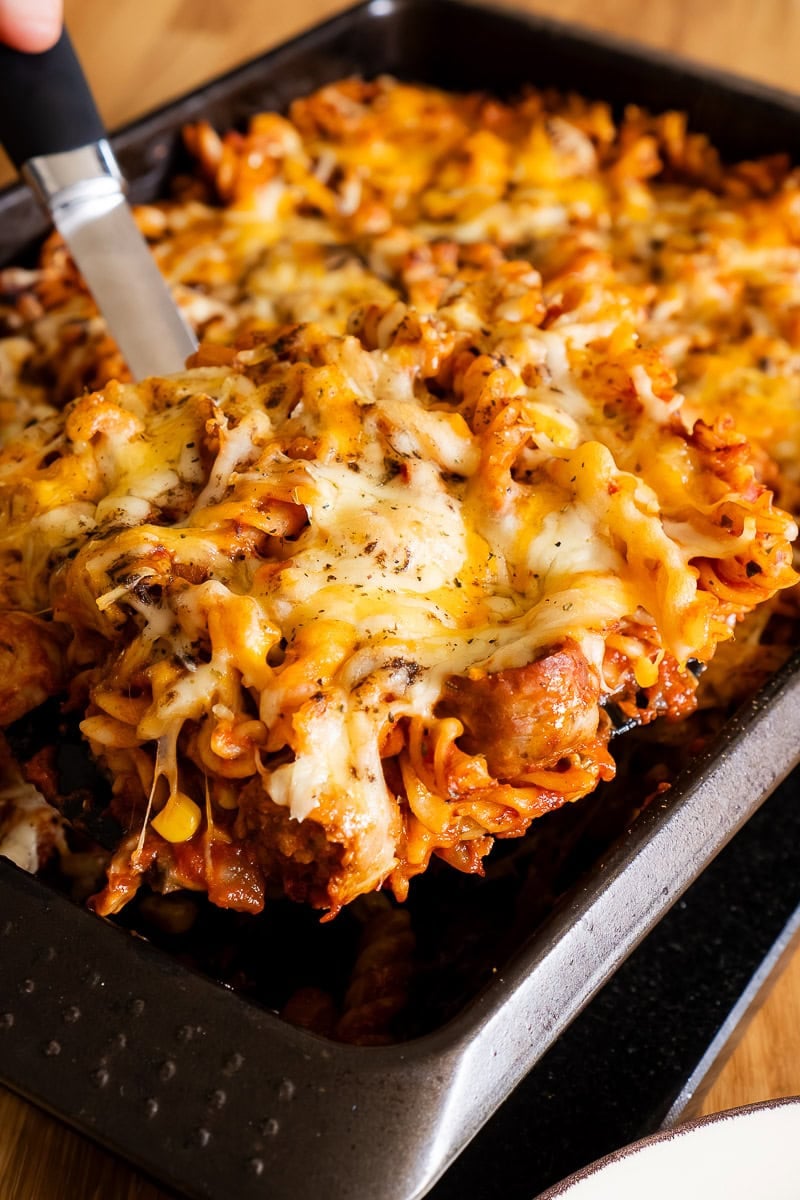 Sausage tray bake Pasta being picked up with a large spatula