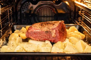 Top rump beef sitting on onion quarters with roast potatoes arranged around the roasting tray before cooking.